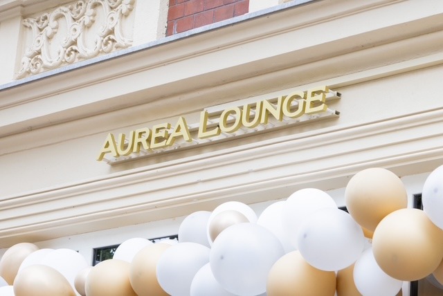 Goldener Auréa-Lounge-Schriftzug über dem Eingang, davor Luftballons