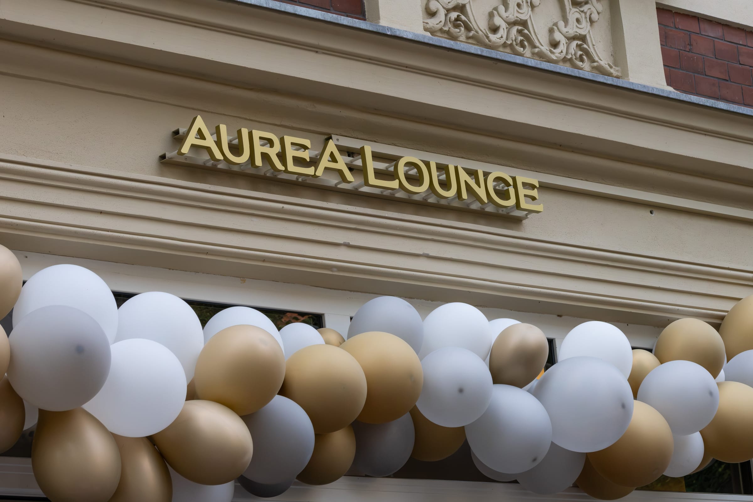 Goldener Auréa-Lounge-Schriftzug an der Fassade, darunter weiße und goldene Luftballons