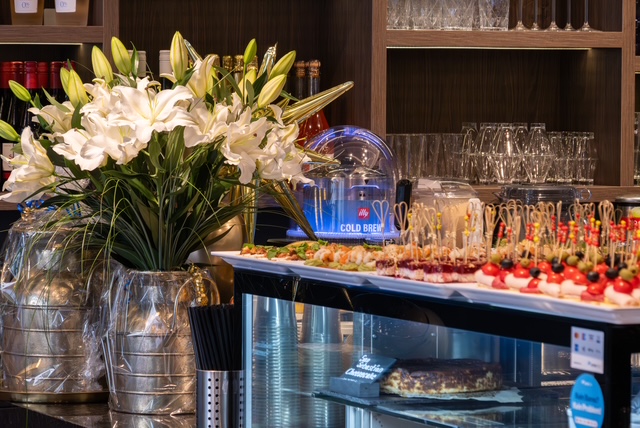 Die Bar der Auréa Lounge: weiße Lilien und Fingerfood auf der Theke, dahinter Gläser im Regal